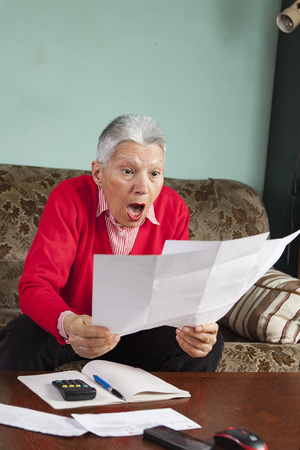 Senior old woman shocked with the bills she receives, appalled and gaspingの写真素材