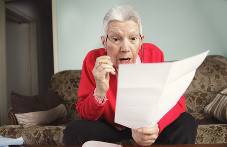 Senior old woman shocked with the bills she receives, appalled and gaspingの写真素材