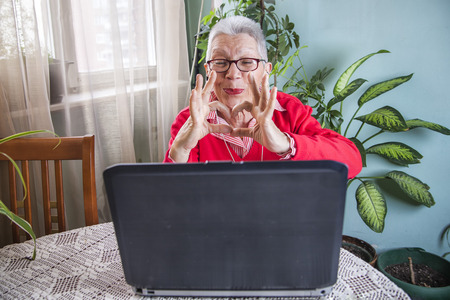 Senior old woman sending love and kisses to her family over social media apps using her laptopの写真素材