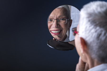 Senior elderly woman applying make up, looking herself at a hand mirrorの写真素材
