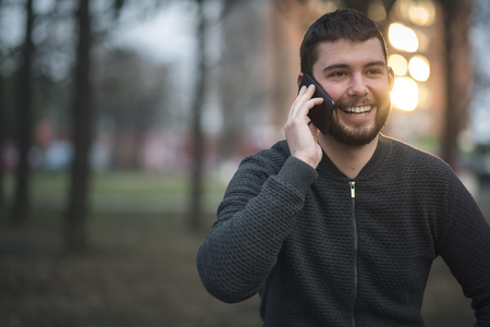 Young mid-twenties man talking on his cell phone, speaking with a friend as hes taking a walk in a parkの写真素材
