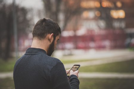 Young mid-twenties man sending a text message on his cell phone, speaking with a friend as hes...