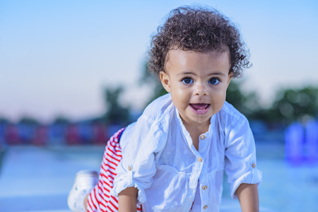 Mixed race baby girl playing next to a fountain sprinkler, enjoying a warm day outside on sunset
