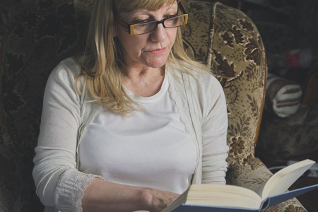 Senior elderly lady reading her favorite book, relaxing at her homeの写真素材