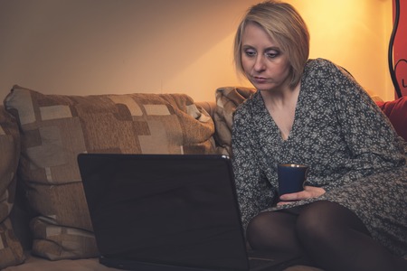 Attractive mature woman relaxing on a sofa and browsing internet on her laptopの写真素材