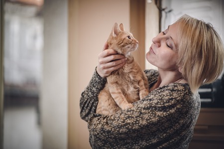 Mature blond woman petting her yellow striped catの写真素材