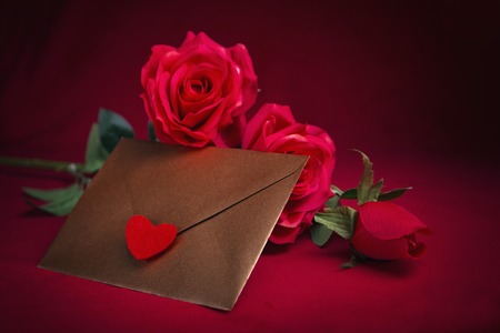 Valentines day celebration with romantic items: sealed love letter, a rose, a heart cup on a dark red backgroundの写真素材