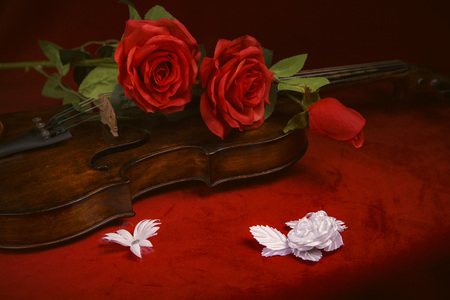 Romance and valentines day concept: old antique violin with lush red roses, on a dark red backgroundの写真素材