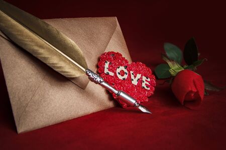 Heart writings, golden quill for the most beautiful poems and words, envelope, quill on a dark red backgroundの写真素材
