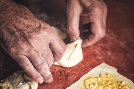 Senior old man hands wrapping small pastry dough with cheeseの写真素材