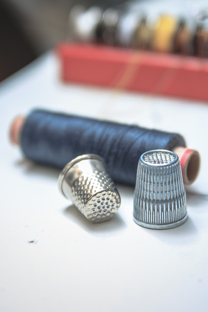 Spools of thread and basic sewing tools including pins, needle, a thimble, and tape measure on a wooden tabletopの写真素材