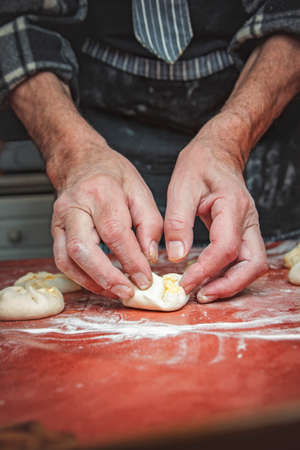 Senior old man hands wrapping small pastry dough with cheese, preparing wonderful baking