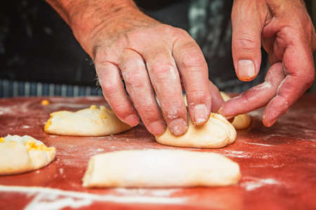 Senior old man hands wrapping small pastry dough with cheese, preparing wonderful baking