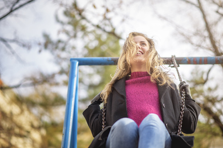 Cute young woman swinging on a park swing, feeling playful and childishの写真素材