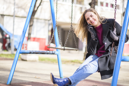 Young woman talking on her cell phone while playing outside on a swing in a parkの写真素材