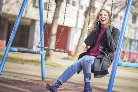 Young woman talking on her cell phone while playing outside on a swing in a parkの写真素材