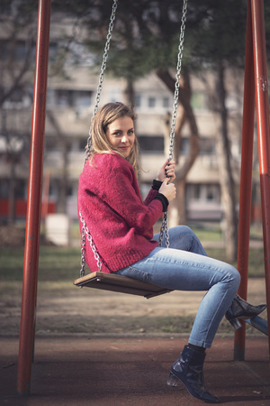 Cute young woman swinging on a park swing, feeling playful and childishの写真素材