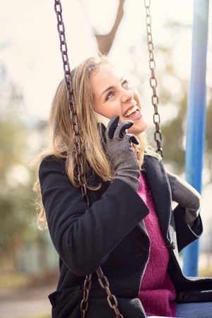 Young woman talking on her cell phone while playing outside on a swing in a parkの写真素材