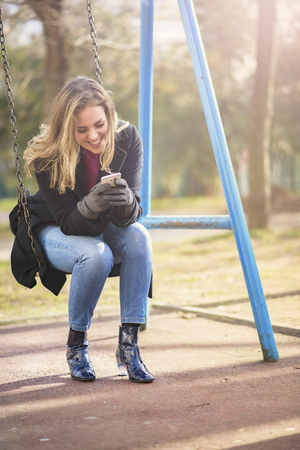 Young woman talking on her cell phone while playing outside on a swing in a parkの写真素材
