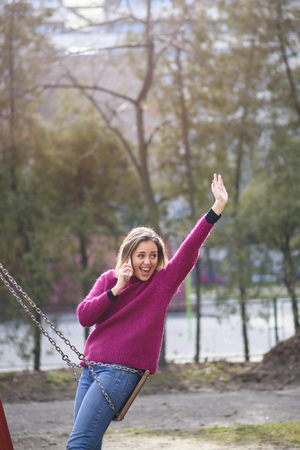 Sweet young woman saying hello to a an acquaintance while talking on her cell phone, park and outdoors sceneの写真素材
