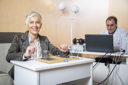 Senior woman checking her health status at the clinic, undergoing quantum and bioresonant medical examの写真素材