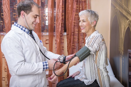 Elderly lady having her blood pressure checked with her doctor in a friendly clinic or a hospitalの写真素材