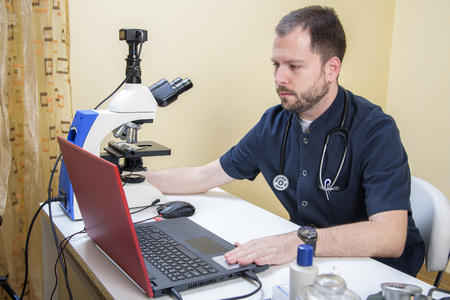 Young handsome doctor checking the blood sample on his microscope in his medical officeの写真素材