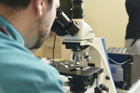 Young handsome doctor checking the blood sample on his microscope in his medical officeの写真素材