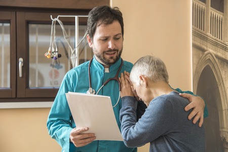 Depressed senior woman, a patient of a young doctor, crying on his shoulder upon hearing bad newsの写真素材