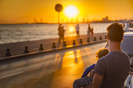 AUGUST 2017, THESSALONIKI GREECE: Young father holding his child, enjoying a sunset view from the shoreのeditorial素材