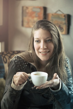 Cheerful young casual lady drinking her coffee in a coffee shop, enjoying some free time for herselfの写真素材