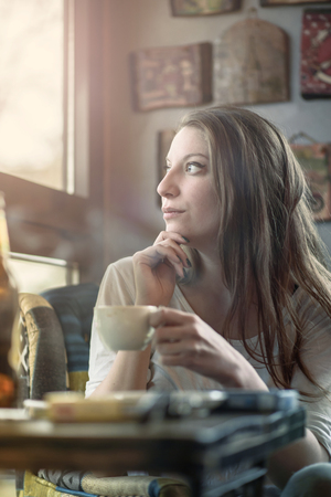 Cheerful young casual lady drinking her coffee in a coffee shop, enjoying some free time for herselfの写真素材