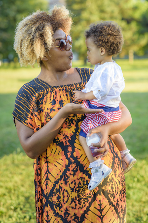 Mother and daughter, african american and mixed race, playing together in a park on a bright sunny dayの写真素材
