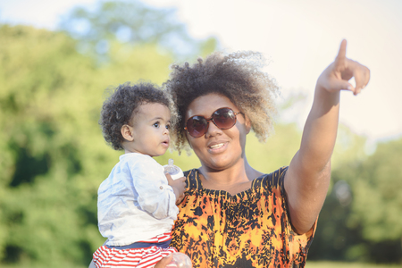 Mother and daughter, african american and mixed race, playing together in a park, mom showing her daughter something in the skyの写真素材