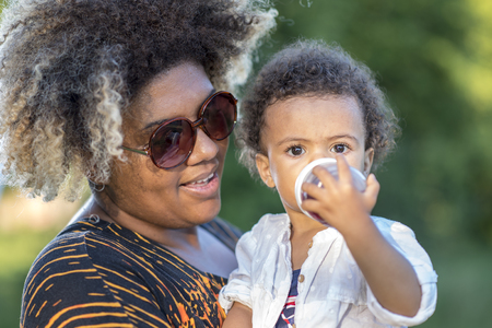 Mother and daughter, african american and mixed race, playing together in a park on a bright sunny dayの写真素材