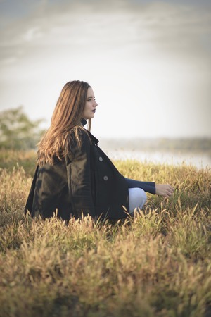 Thoughtful sad, melancholic girl sitting in the grass, running through her memoriesの写真素材