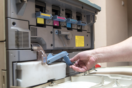 Hand of a man replacing ink cartridge on a professional printing machine