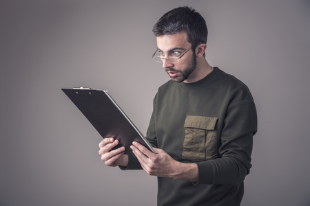 Young man is in shock with his finances and reports, holding his spectacles