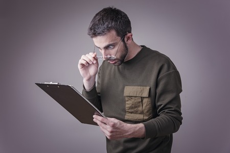 Young man is in shock with his finances and reports, holding his spectaclesの写真素材