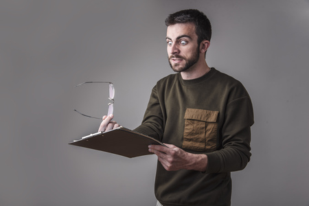 Young man is in shock with his finances and reports, holding his spectaclesの写真素材