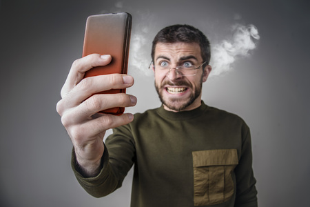Young man angry with his cell phone, yelling at it, letting off steam and burning his phone with...