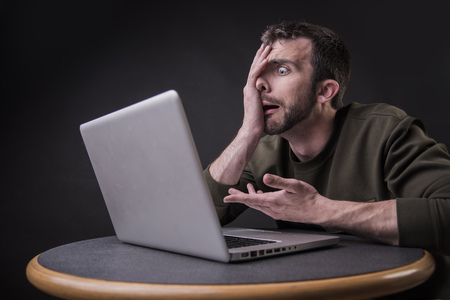 Young man shocked and surprised with the content he sees on his laptopの写真素材