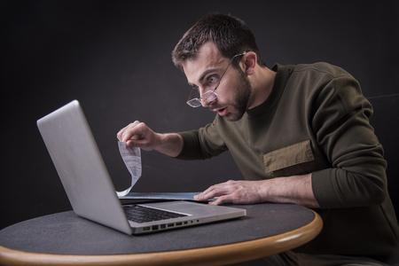 Young man is in shock with his finances and reports, screaming at his laptopの写真素材