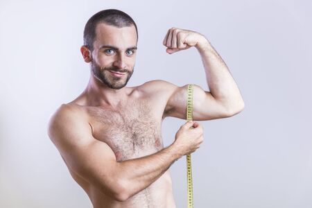 Young shirtless man measuring his biceps sizeの写真素材