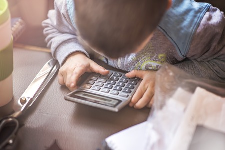 Cute little toddler boy using a calculator, figuring out a math problem, developing logic skillsの写真素材