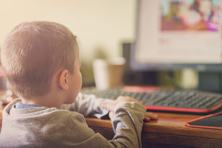 Cute little toddler boy sitting at the desk, watching a video on a desktop computerの写真素材
