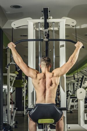 Shoulder pull down machine. Fitness man working out lat pulldown training at gym. Upper body...