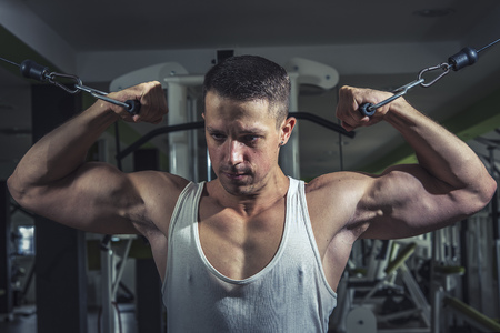 Young caucasian athletic man in the gym doing cable fly exercises