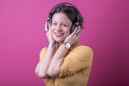 Trendy young woman enjoying her favorite music on big headphones, pink magenta backgroundの写真素材