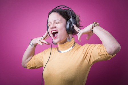 Trendy young woman enjoying her favorite music on big headphones, pink magenta backgroundの写真素材